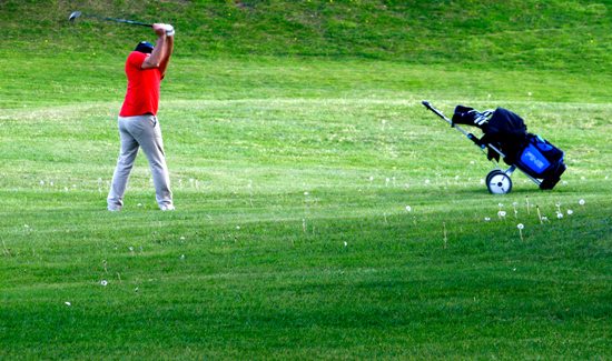 Imagen de un golfista en medio de un pradera haciendo un swing de golf